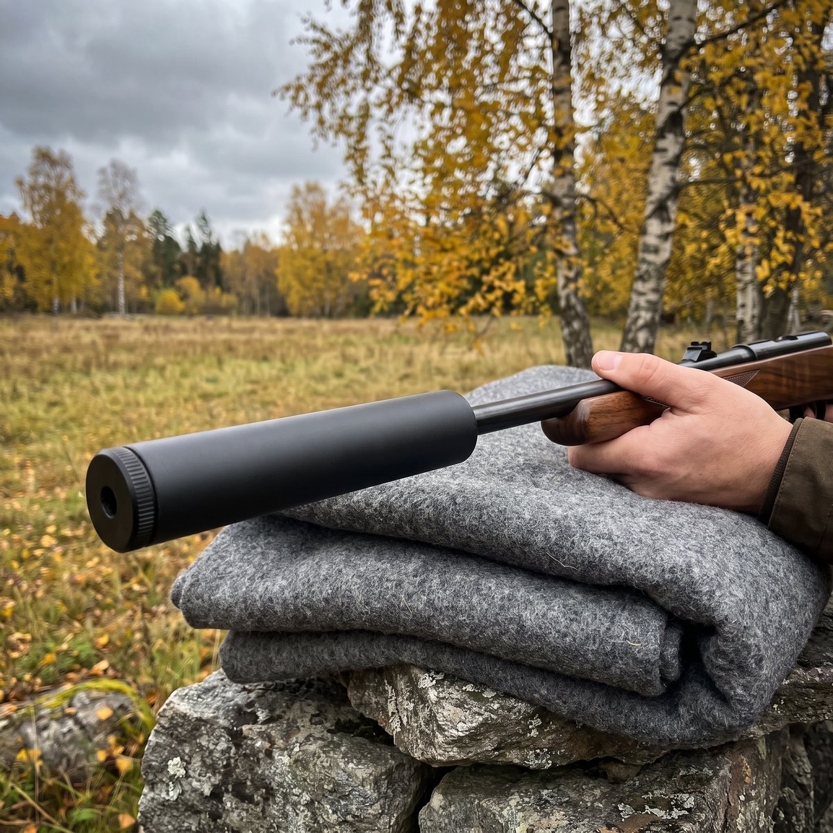 Jaki 22LR ljuddämpare på ett salongsgevär med trästock, vilande på en ullfilt på en stenmur vid en höstäng med björkar
