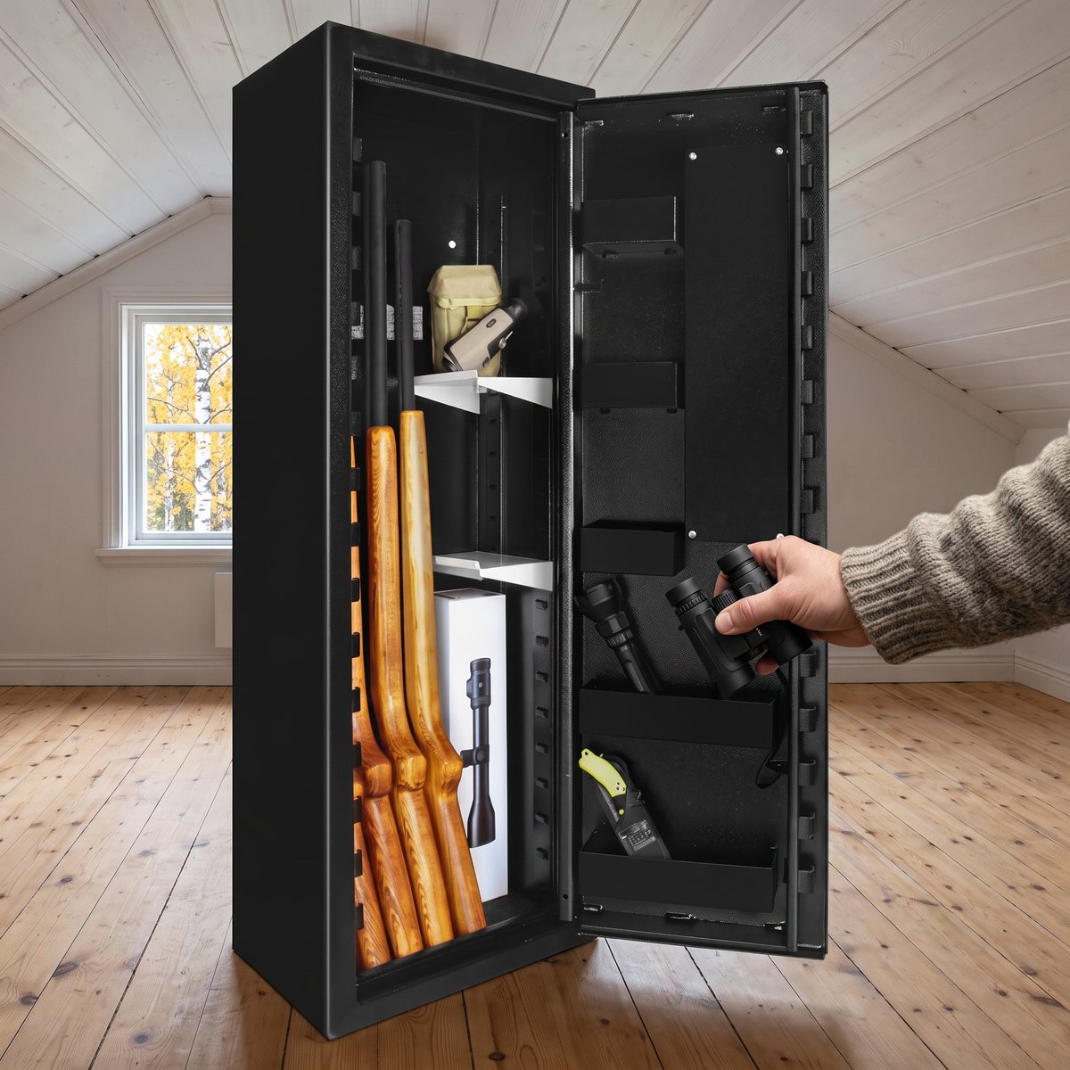 Svart vapenskåp Scandinavian Safe SP66 med öppen dörr på ett vindsrum med trägolv, där en hand tar en kikare från en av dörrhyllorna