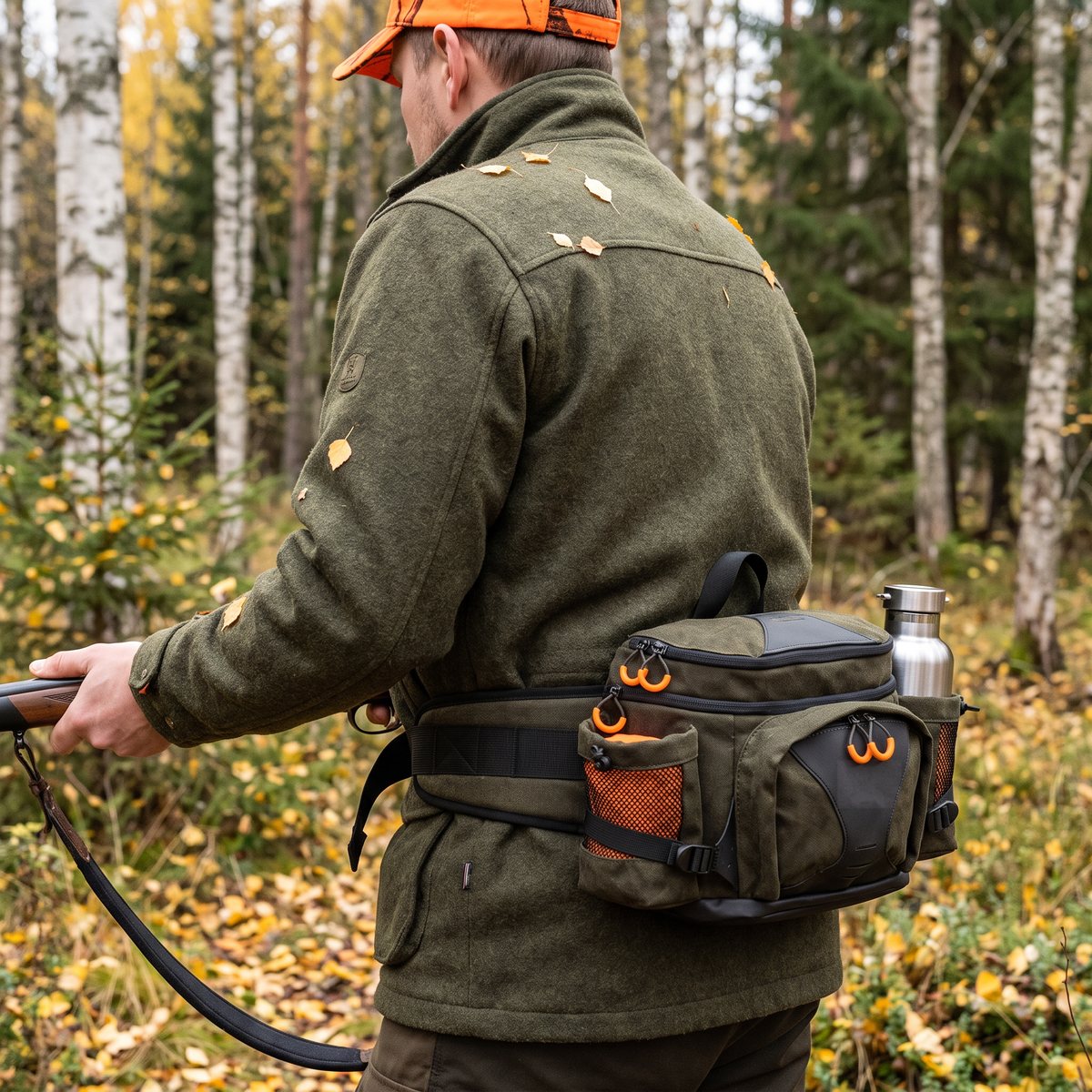 Fauna F12 midjeväska i grönt med orange detaljer och vattenflaska i sidofickan, buren på höften under drevjakt i en svensk björkskog