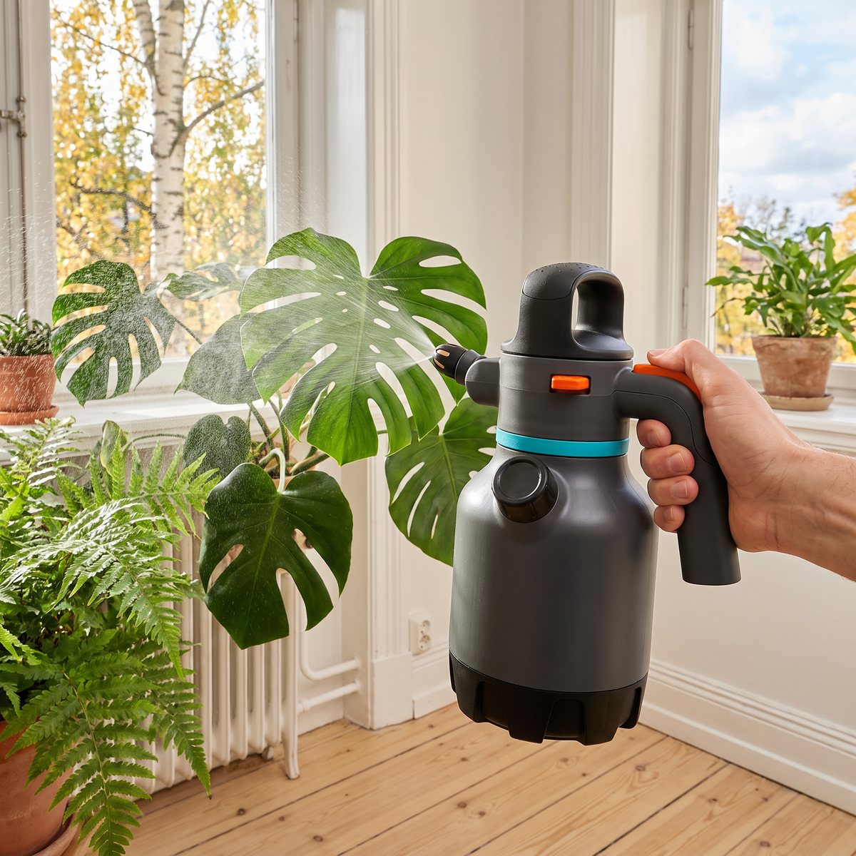 Gardena Tryckspruta 1,25 l i en hand som duschar dimma över monstera och ormbunke i ett ljust svenskt fönster