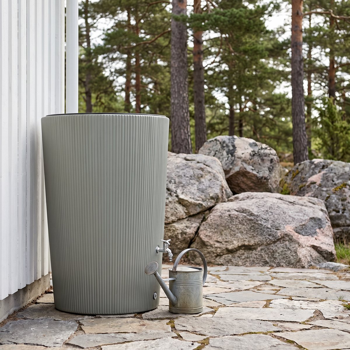 Flexigarden Mälaren räfflad regntunna i salviagrått vid en vit husvägg på en stenlagd uteplats