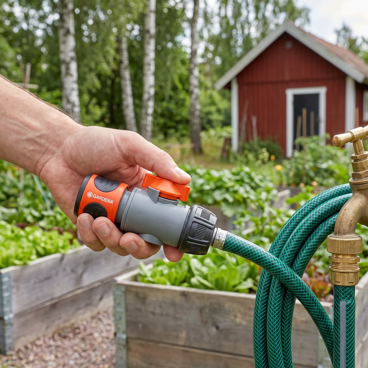 Gardena slangkoppling med reglerventil, handen vrider det orange reglaget i en svensk köksträdgård