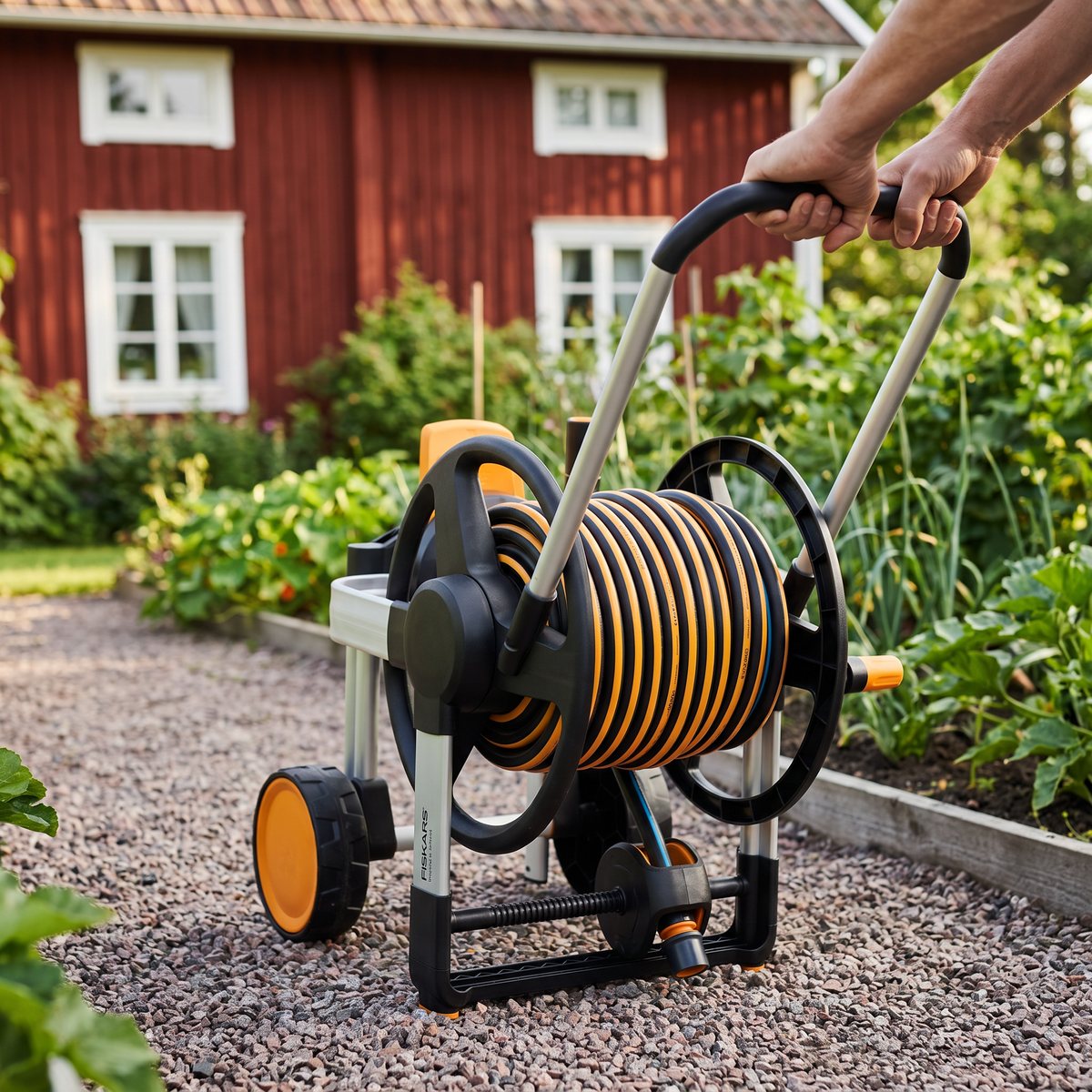Slangvagnen Fiskars Waterwheel XL dras längs en grusgång mot ett grönsaksland i en svensk trädgård