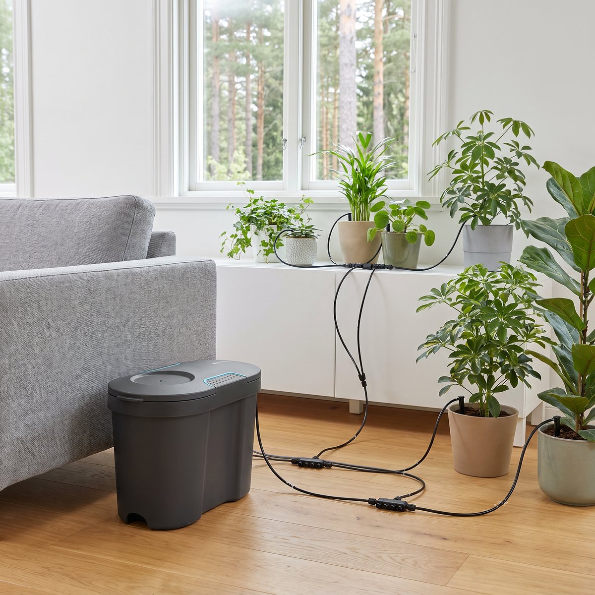 Gardena semesterbevattning med mörk vattentank bredvid soffan och droppslangar till krukväxter i ett svenskt vardagsrum