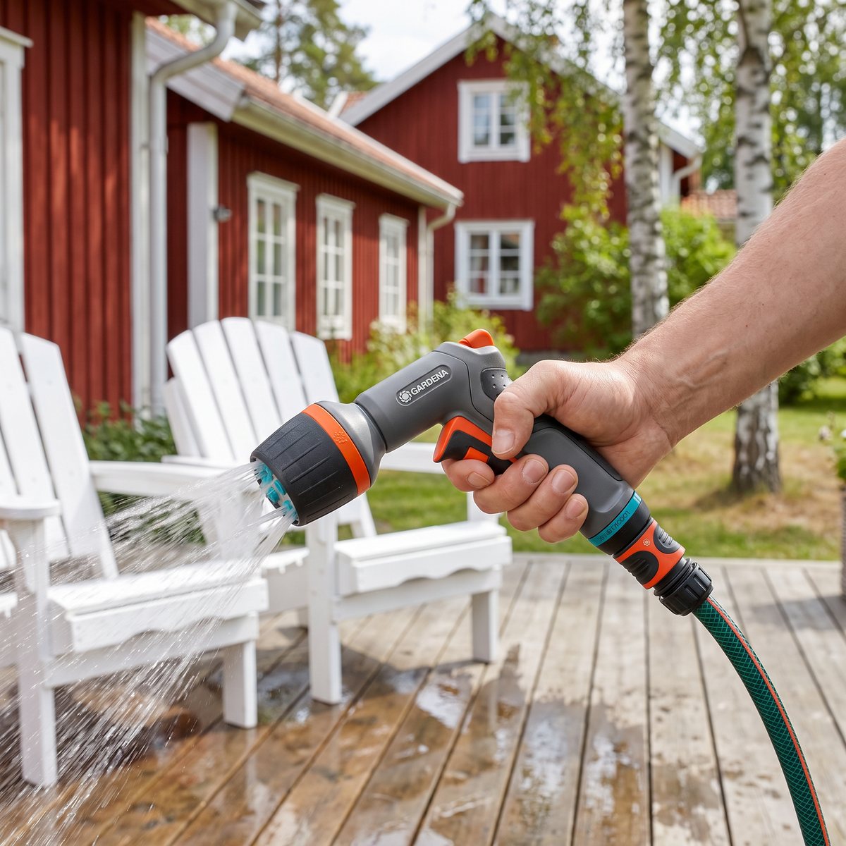 Gardena Comfort ecoPulse strålpistol som spolar en trädäck och vita trädgårdsstolar vid ett rött trähus