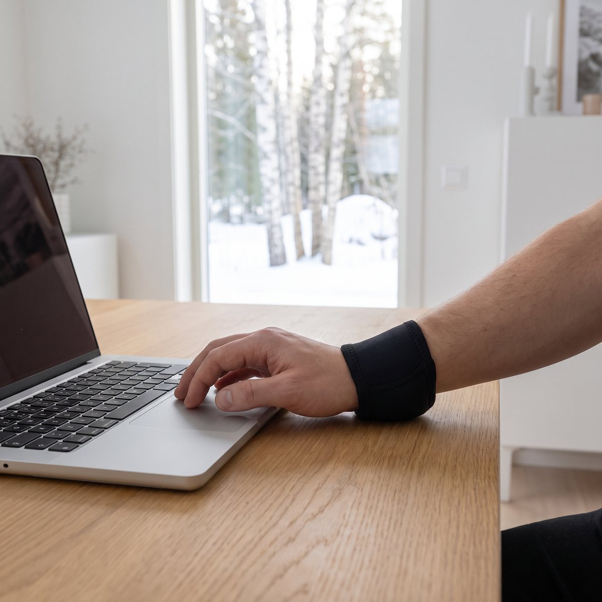 Svart handledsband på handleden vid laptopen vid ett skrivbord i ett svenskt hemmakontor