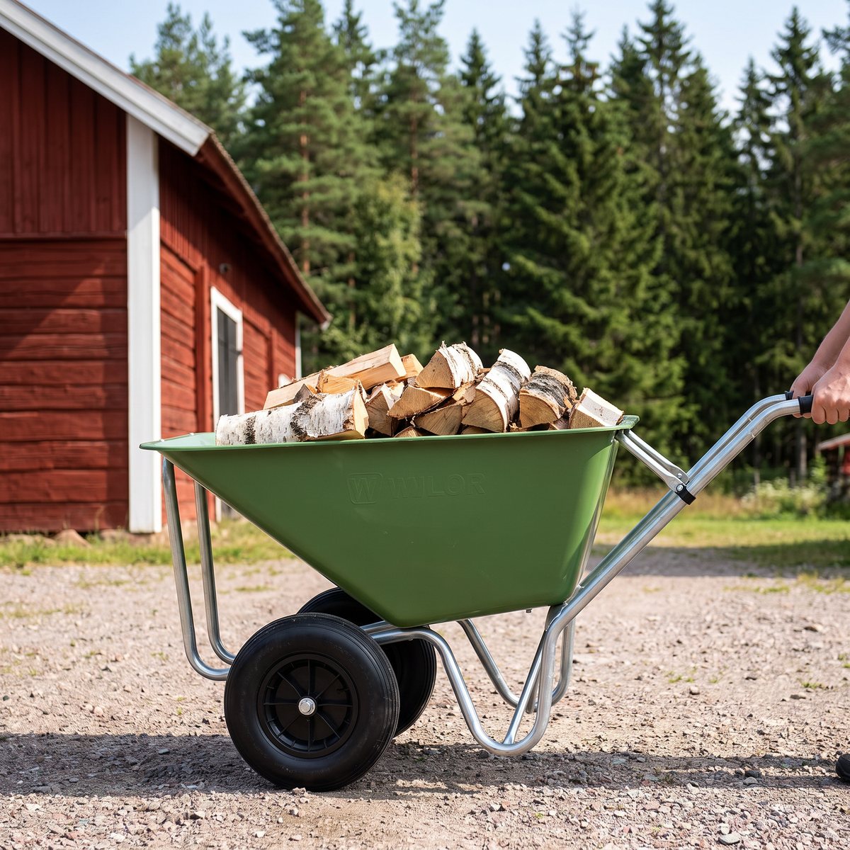 Grön Willab plastkärra med två hjul lastad med ved på en grusplan framför en röd lada