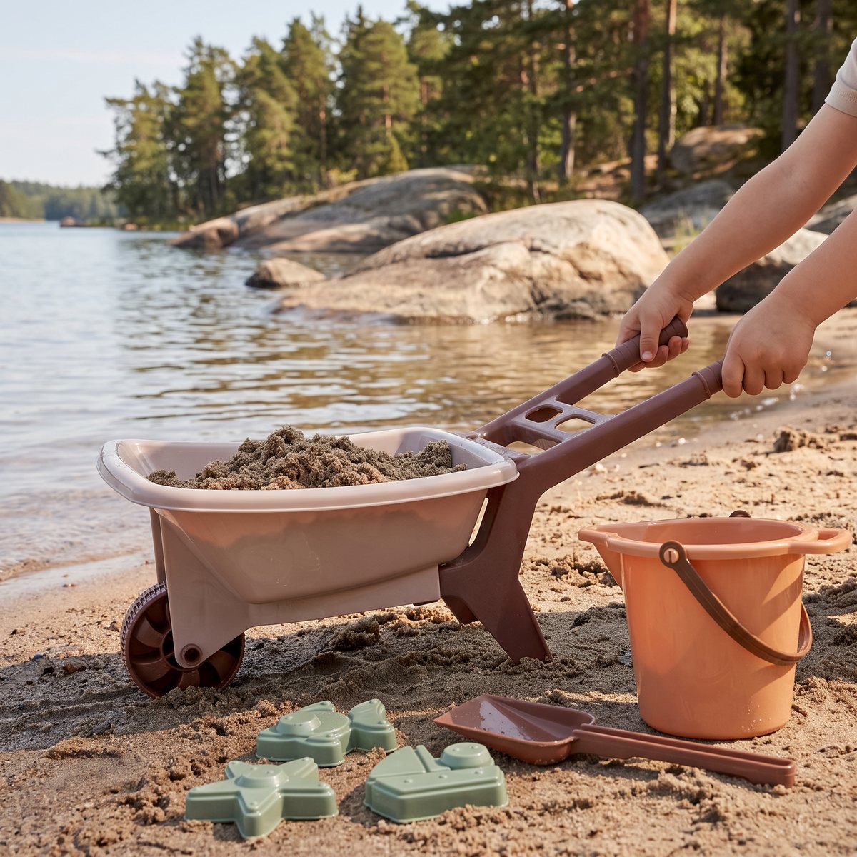 Liten plastkärra med hink, spade och formar fylld med sand på en svensk sjöstrand