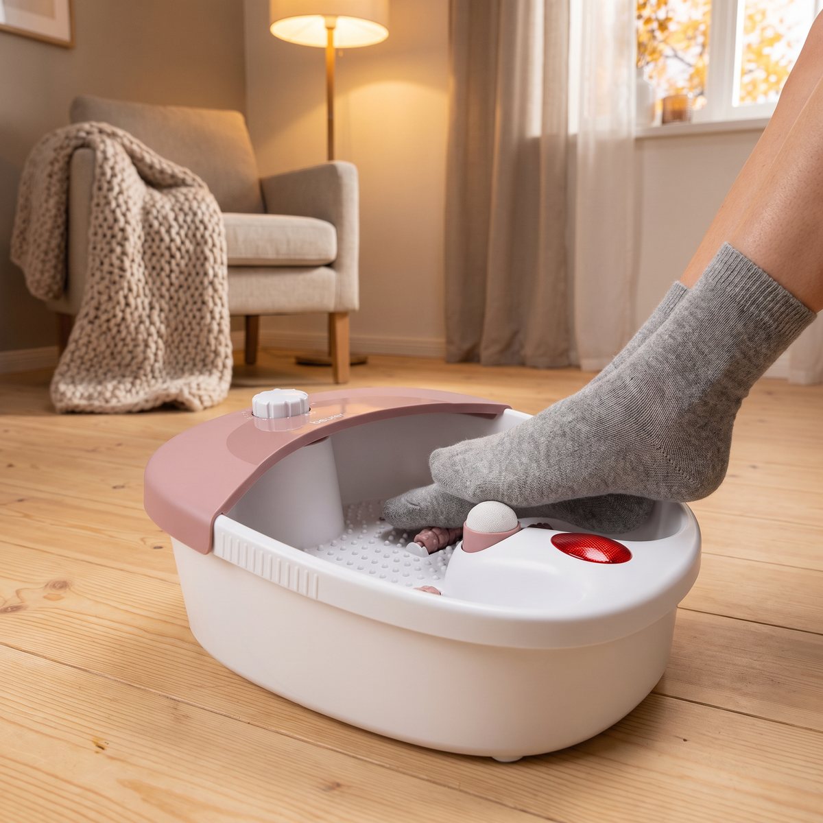 Beurer FB 20 i vitt och rosa utan vatten, med en fot i grå ullsocka på massagerullarna, på ett ljust trägolv i ett svenskt vardagsrum