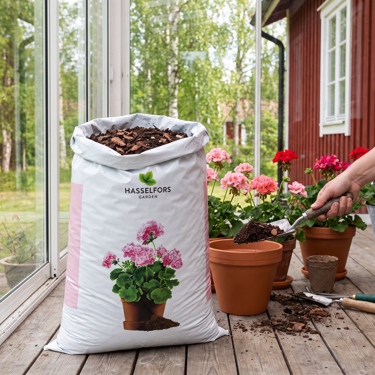 Säck med Hasselfors Mårbacka pelargonjord på en inglasad veranda vid ett rött trähus, där pelargoner planteras i terrakottakrukor