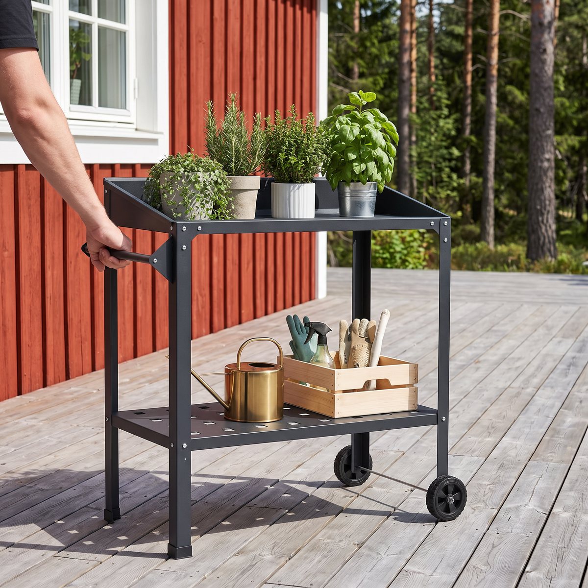 Svart planteringsbord i stål med hjul som rullas i handtaget över ett trädäck vid ett rött trähus