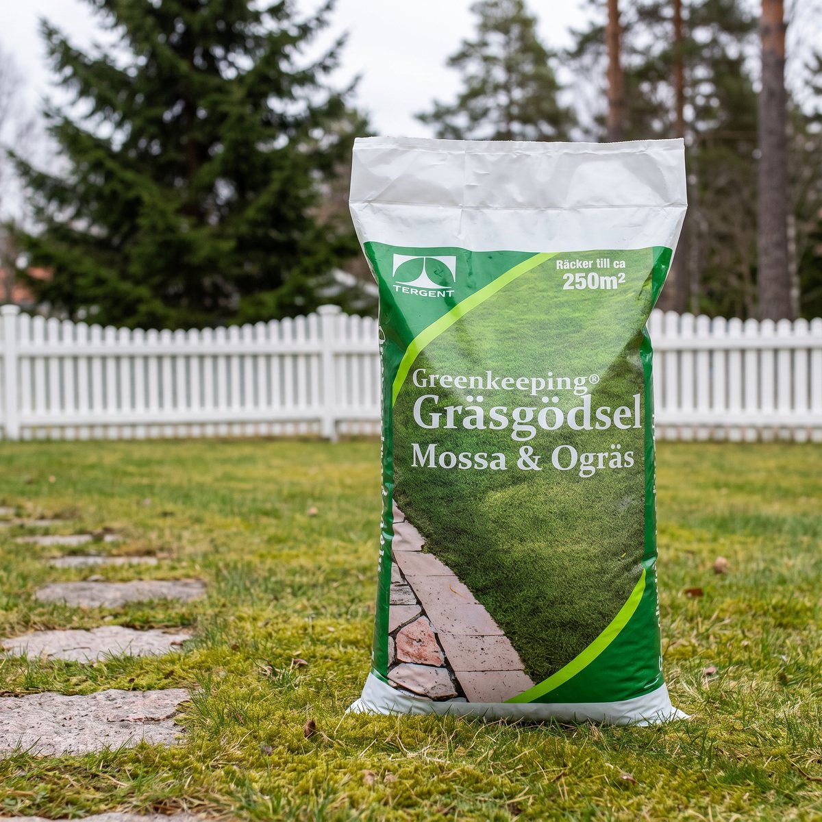 Säck Greenkeeping Gräsgödsel Mossa & Ogräs på en svensk gräsmatta med mossa, stenplattor och vitt staket