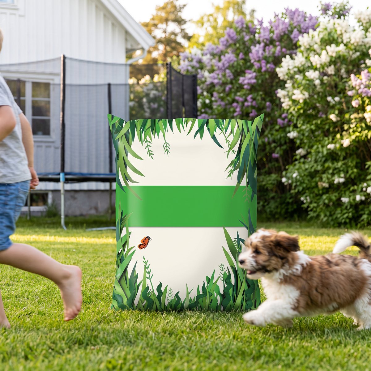 Säck med Algomin Grönare gräsmatta på gräsmattan där ett barn och en hund leker i en svensk trädgård
