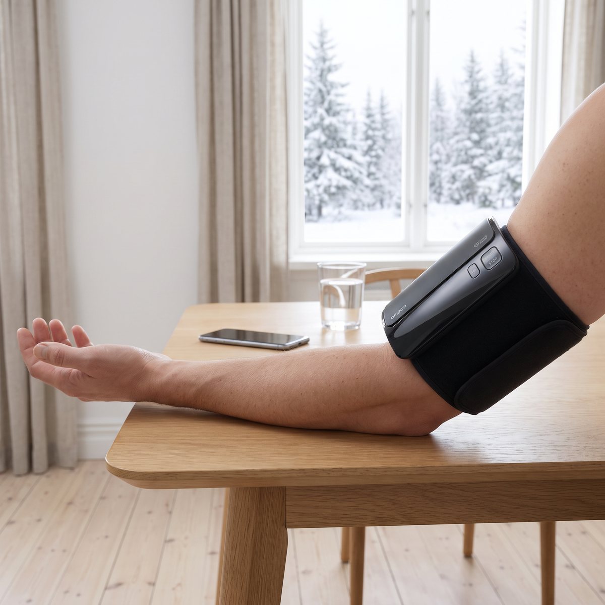 Omron Evolv sitter på överarmen medan underarmen vilar på ett ekbord, med snöig granskog utanför fönstret