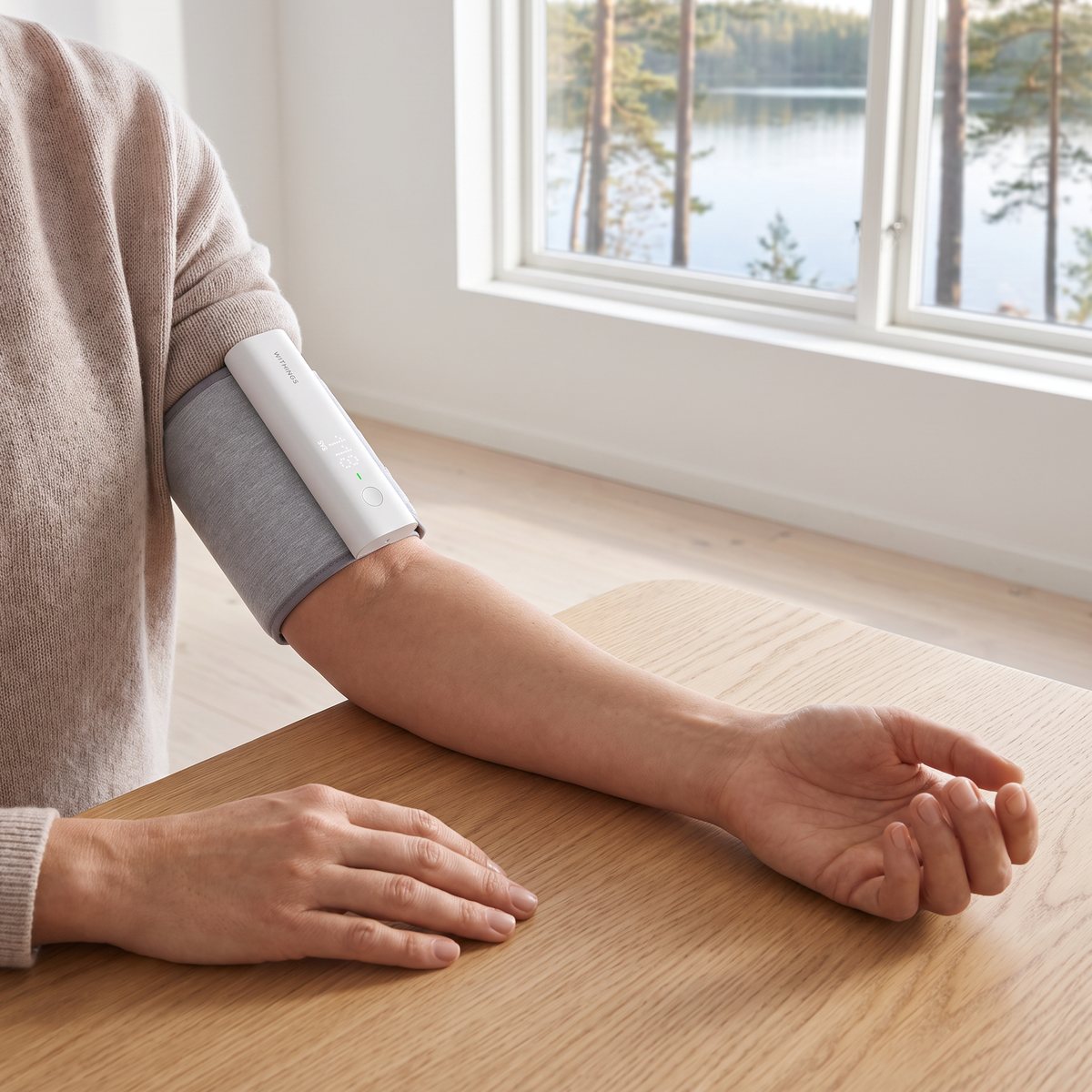 Withings BPM Connect på överarmen medan armen vilar på ett skrivbord vid ett fönster mot en svensk sjö