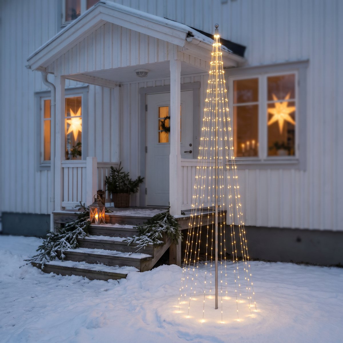 Ljusgran av varmvita lysdioder på en kort stång i snön bredvid entrétrappan till en vit trävilla