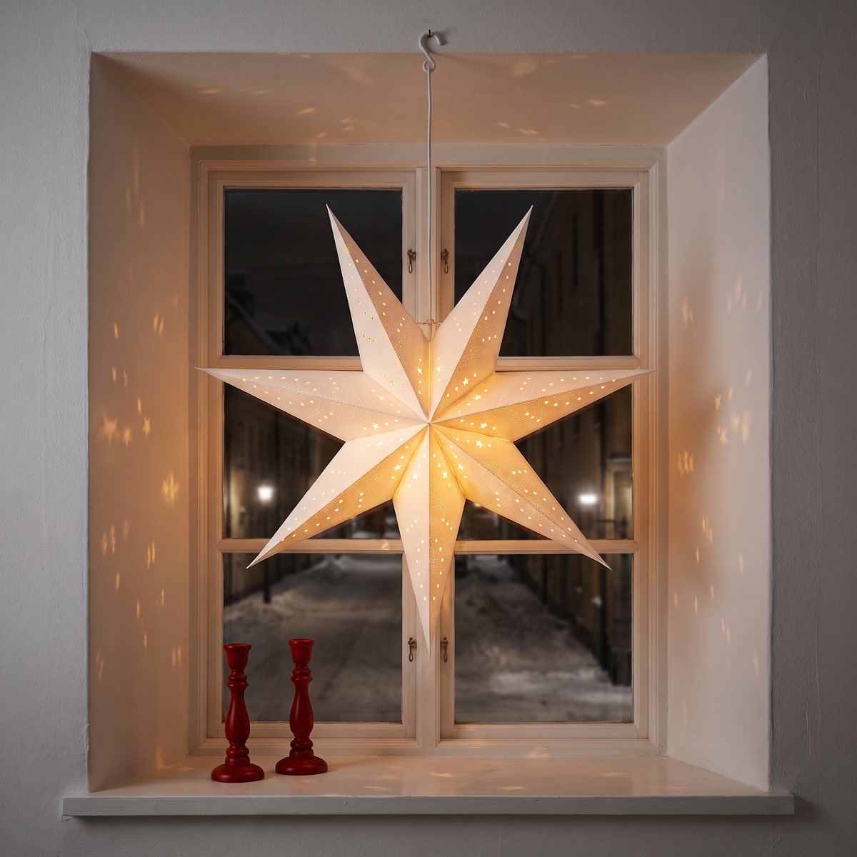 Northlights vita adventsstjärna med hålmönster hänger tänd i en djup fönsternisch och kastar små ljusprickar på väggarna