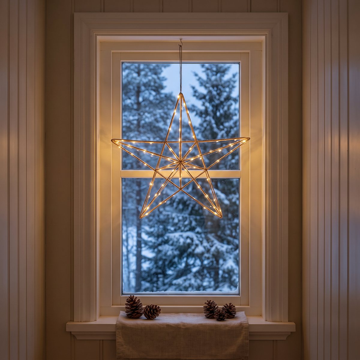 Satanas LED-julstjärna i tunn tråd med små lysdioder hänger i ett litet hallfönster med snöig granskog utanför