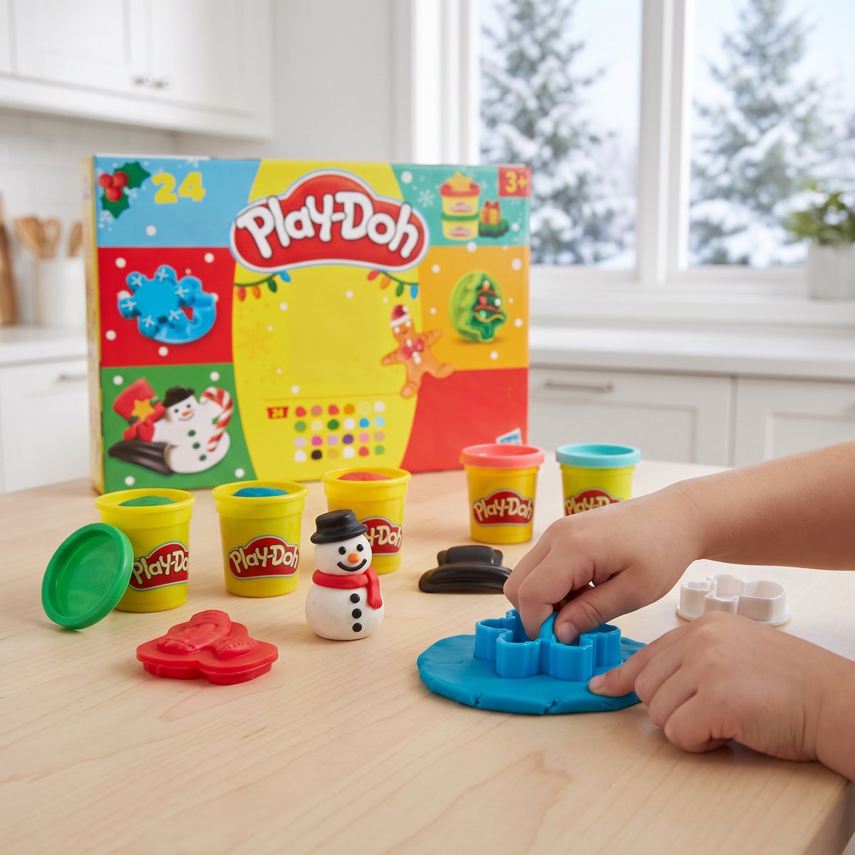 Play-Doh-kalendern på ett köksbord med burkar med lera, en snögubbe av lera och barnhänder som trycker en snöflingeform i blå lera.