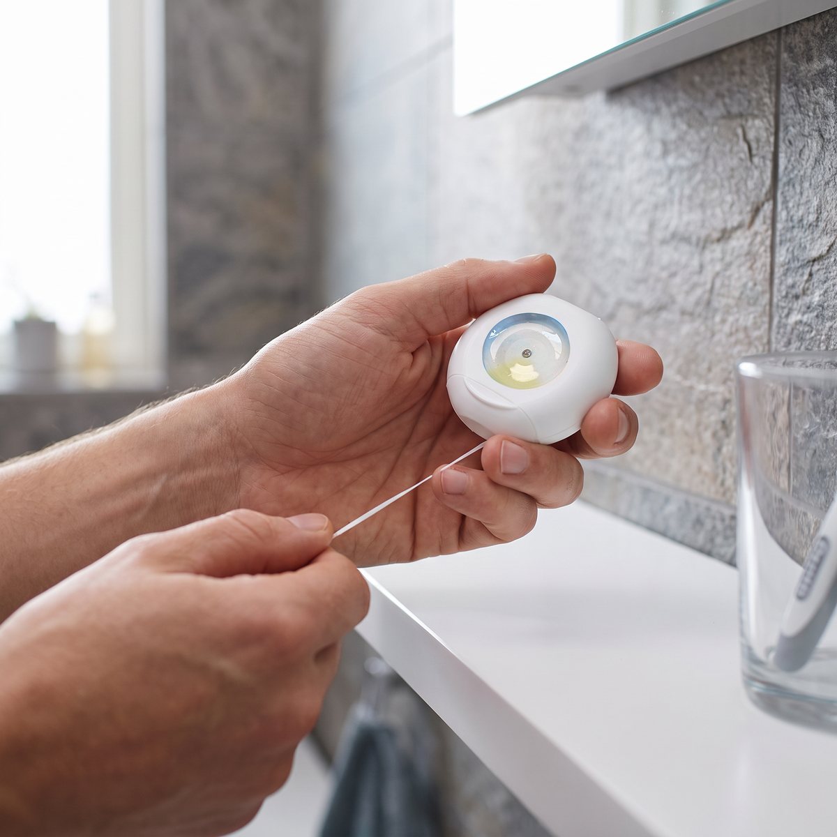 Oral-B Essential Mint dras ut ur den runda dispensern vid en hylla i ett svenskt badrum med stenkakel