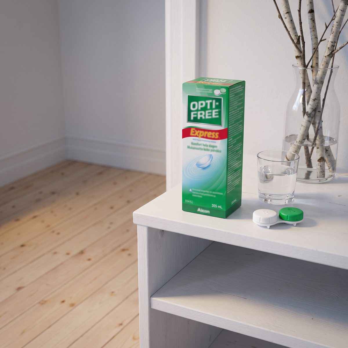 Förpackning Opti-Free Express på en vit hylla bredvid ett glas vatten och ett linsetui i ett svenskt sovrum med björkgrenar