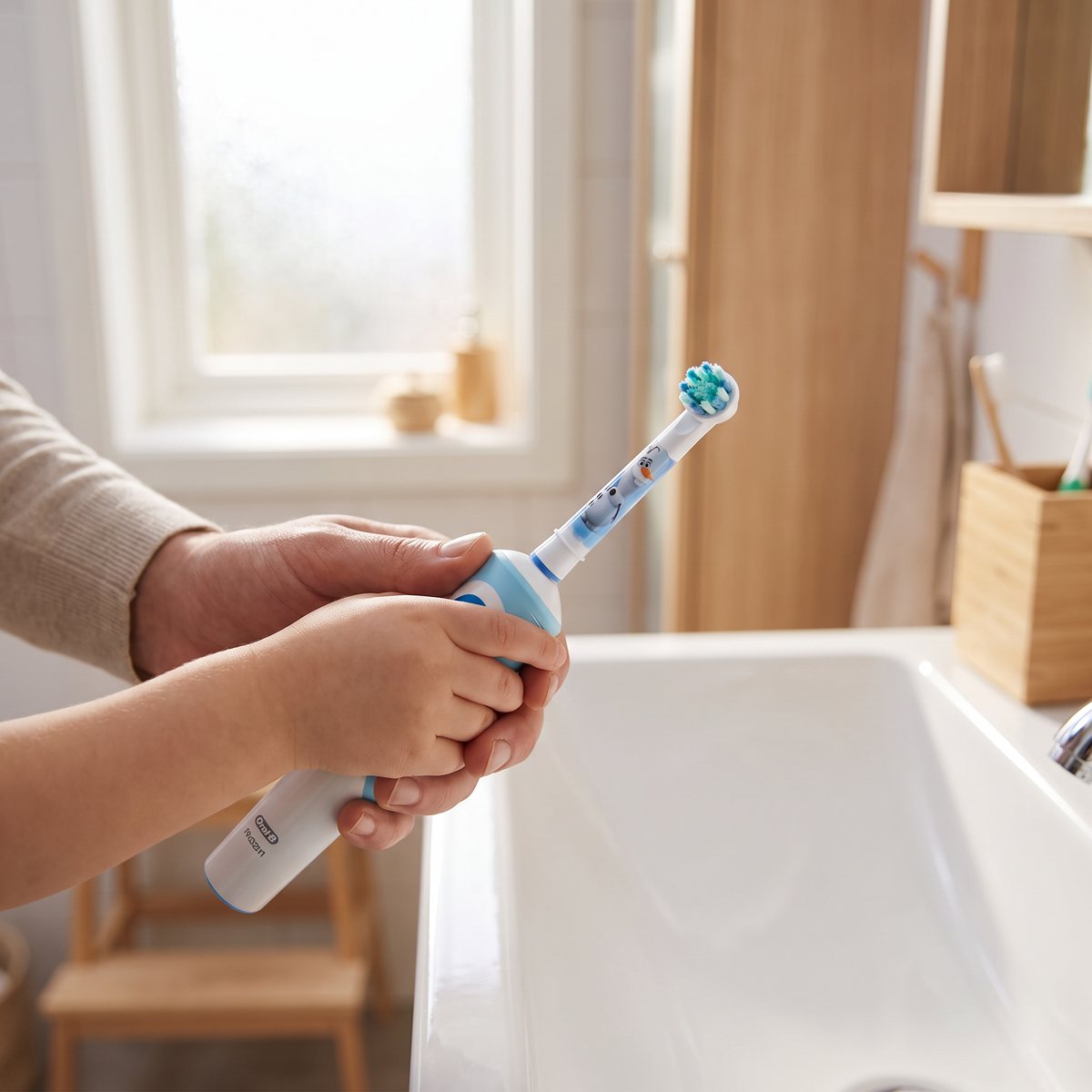 Oral-B Kids-borsthuvud på en eltandborste som en vuxen och ett barn håller tillsammans i ett svenskt badrum