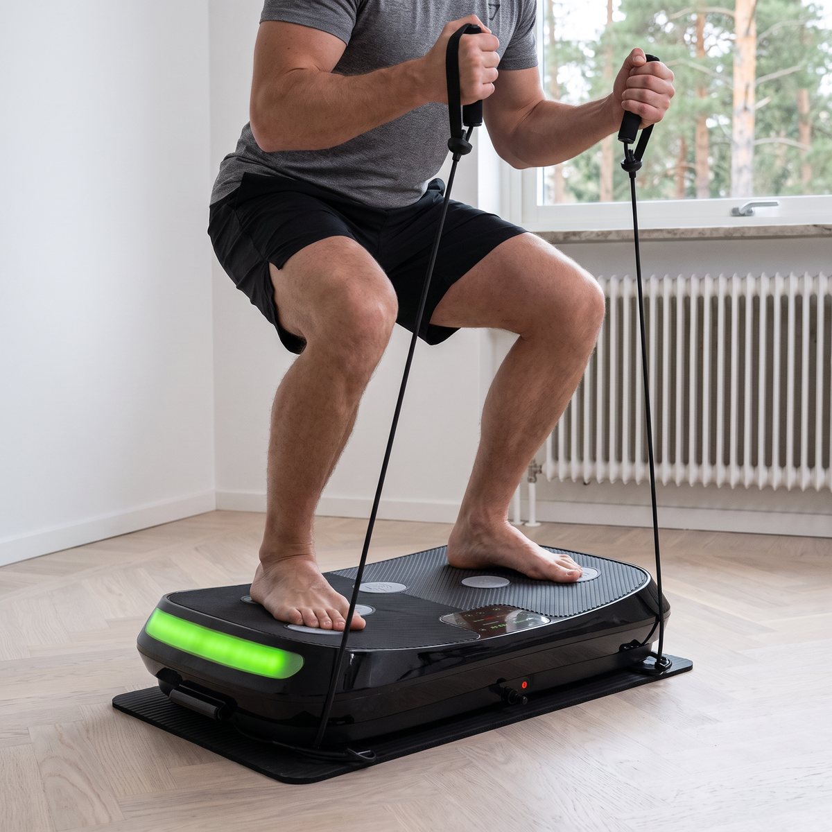 Man i djup knäböj med brett fotavstånd på FitnessPlate 4D med träningsbanden i händerna, i ett svenskt hemmagym med element och tallar utanför