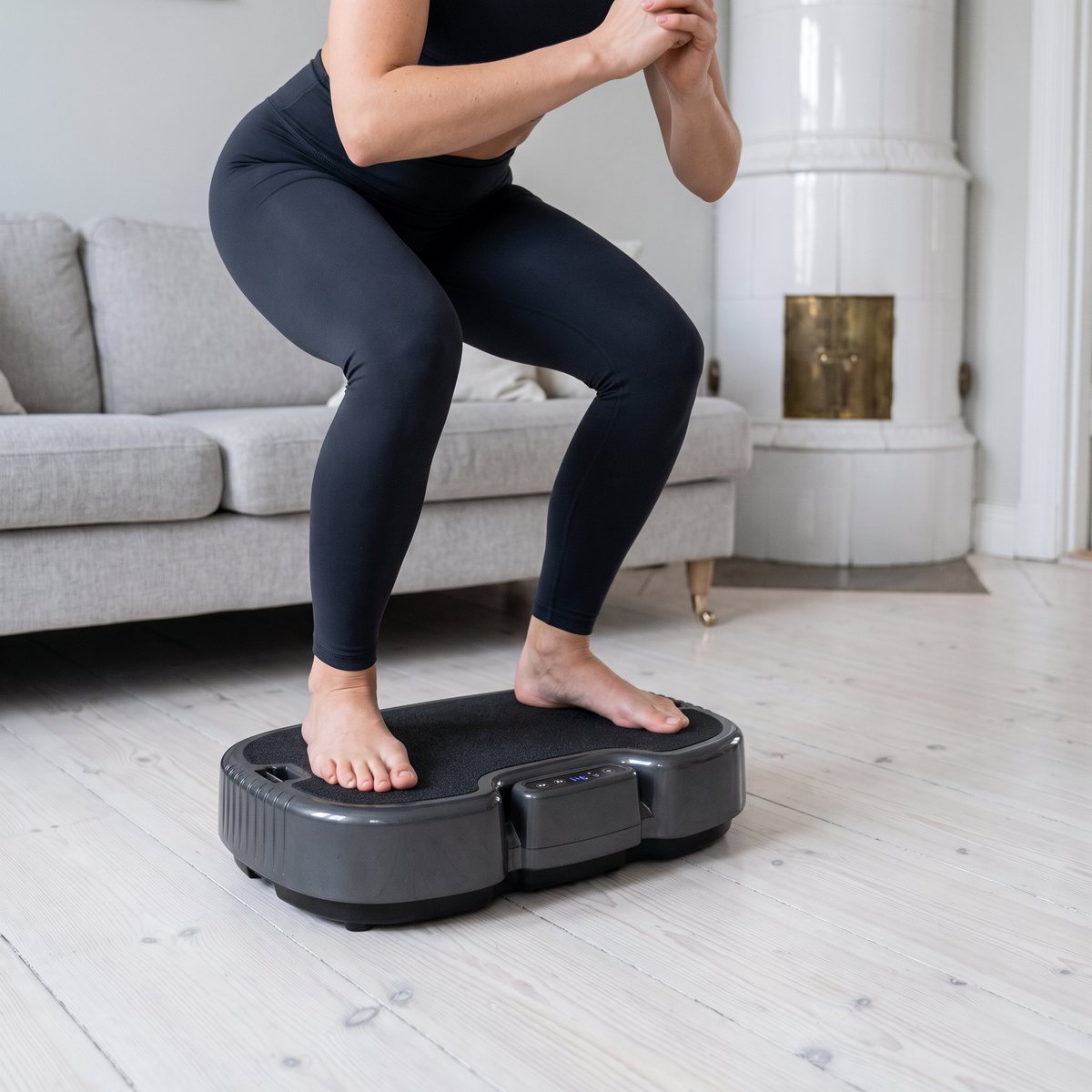 Kvinna håller en statisk knäböj på Power Plate Personal i ett svenskt vardagsrum med kakelugn och vitoljat trägolv