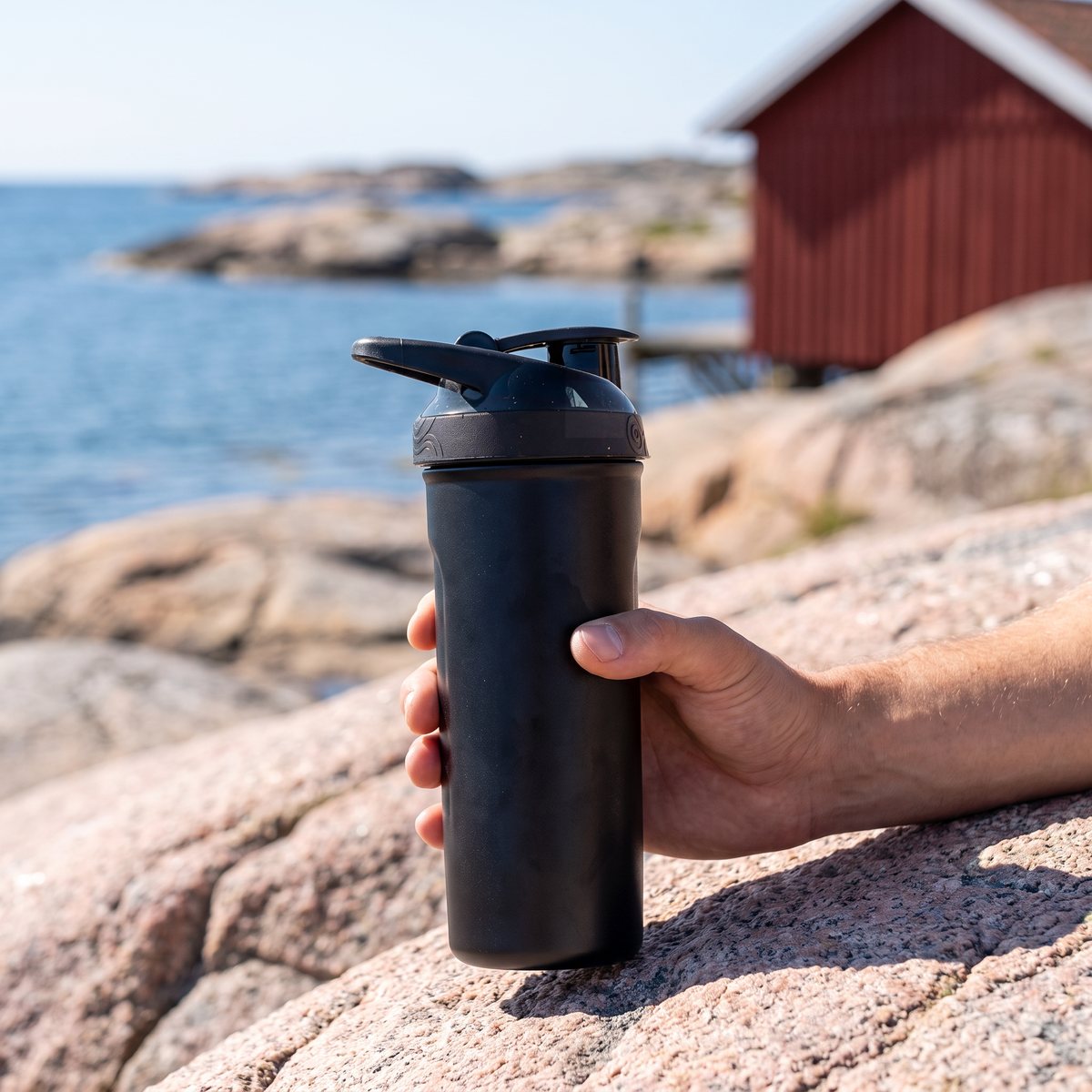 Svart isolerad Smartshake-shaker hålls i handen på granithällar i den svenska skärgården