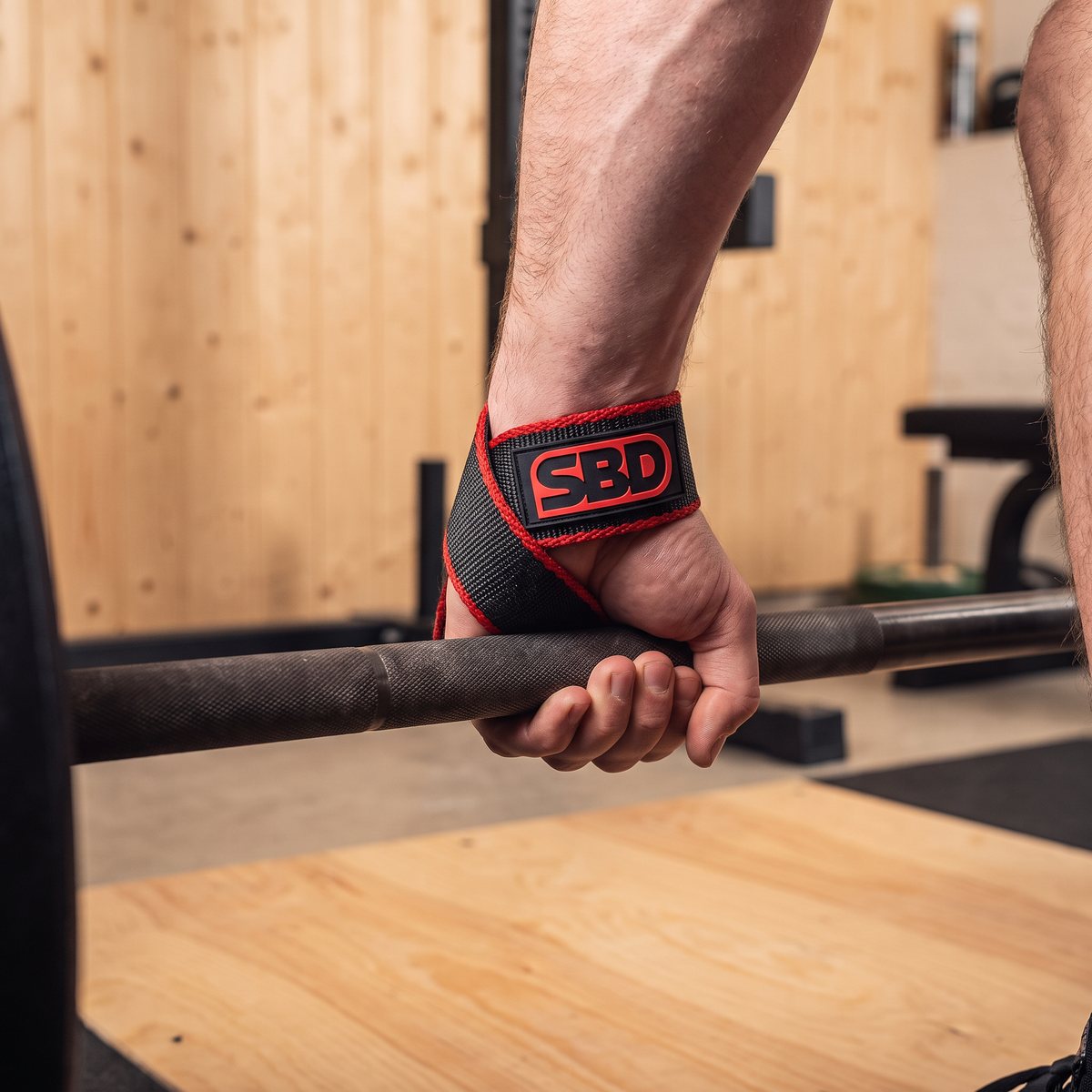 SBD lifting straps i svart och rött virat runt handleden och greppet om skivstången i ett svenskt källargym