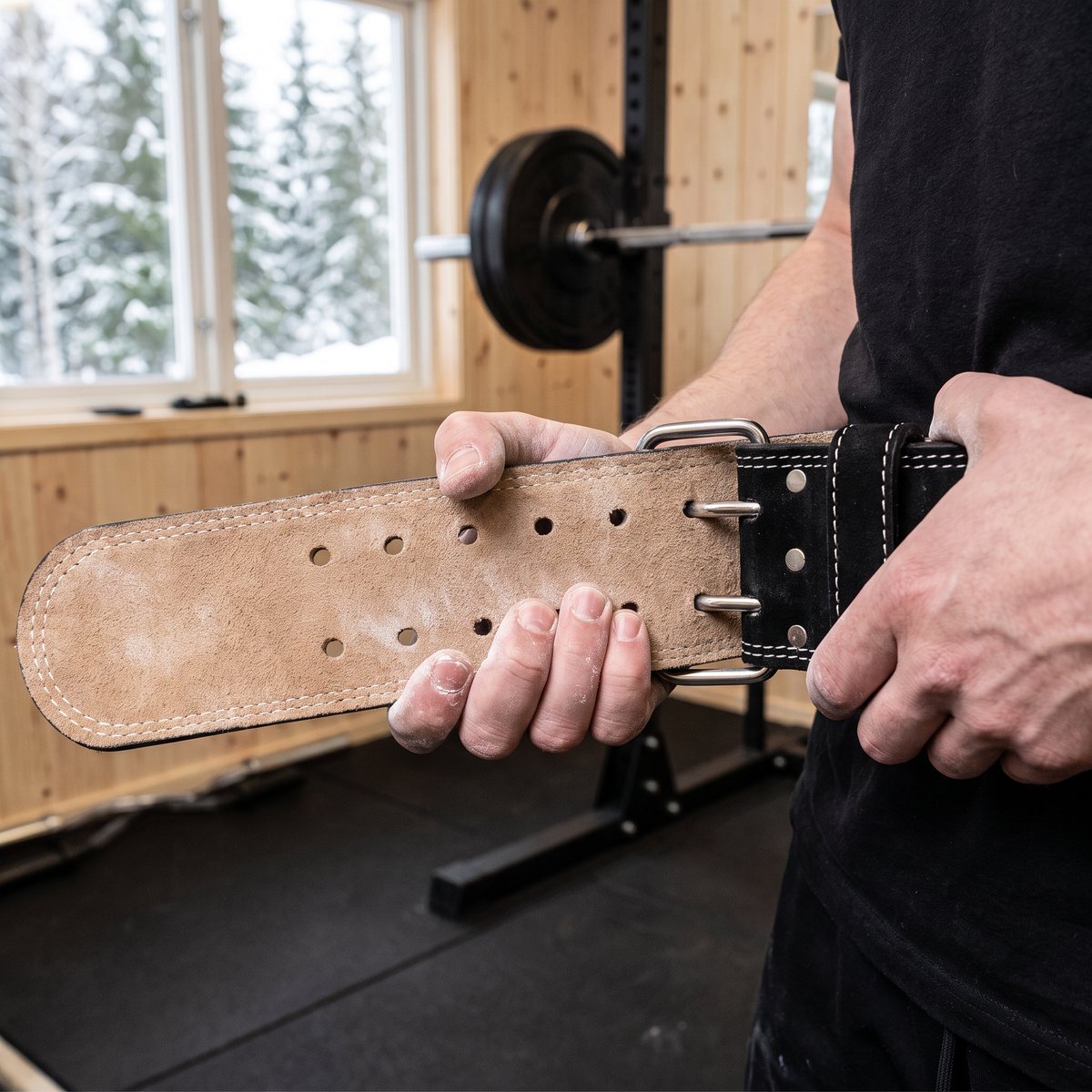 GASP Training Belt med mockainsida och dubbelt dornspänne dras åt med kalkade händer i ett svenskt garagegym med snöig granskog utanför