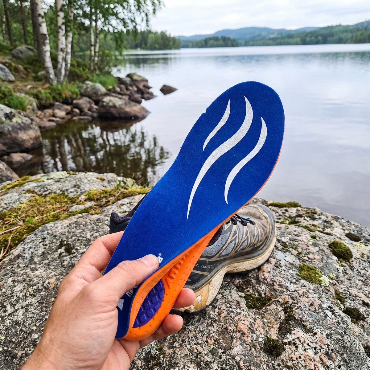 Blå Adapt Sula Sport som hålls vid en löparsko på en sten vid en svensk sjö