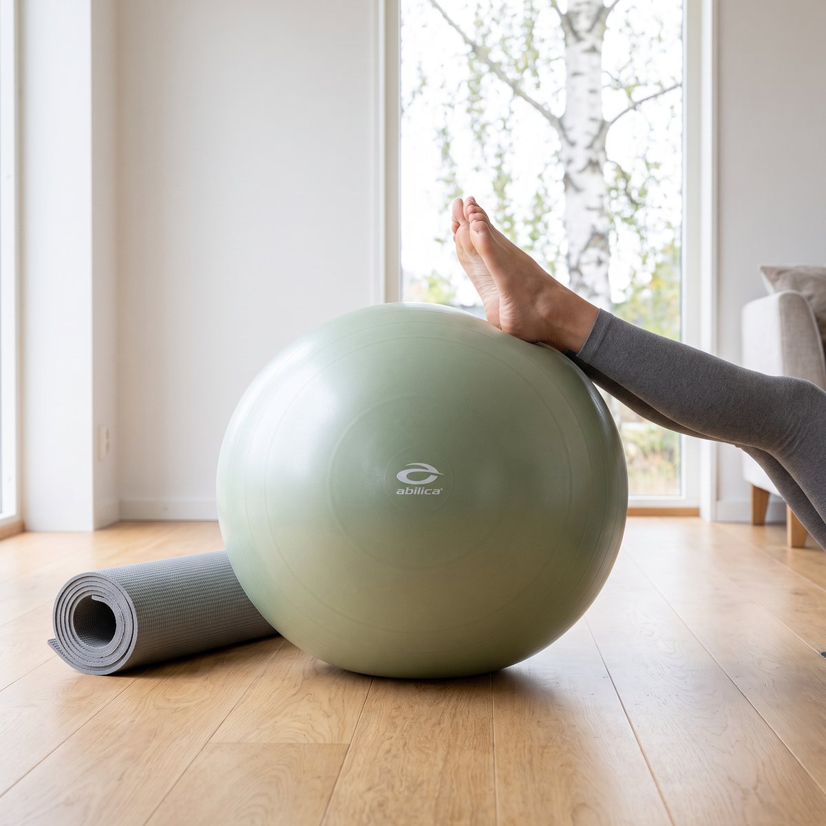 Salviagrön fitnessboll på ljust ekparkett i ett svenskt vardagsrum med björk utanför fönstret