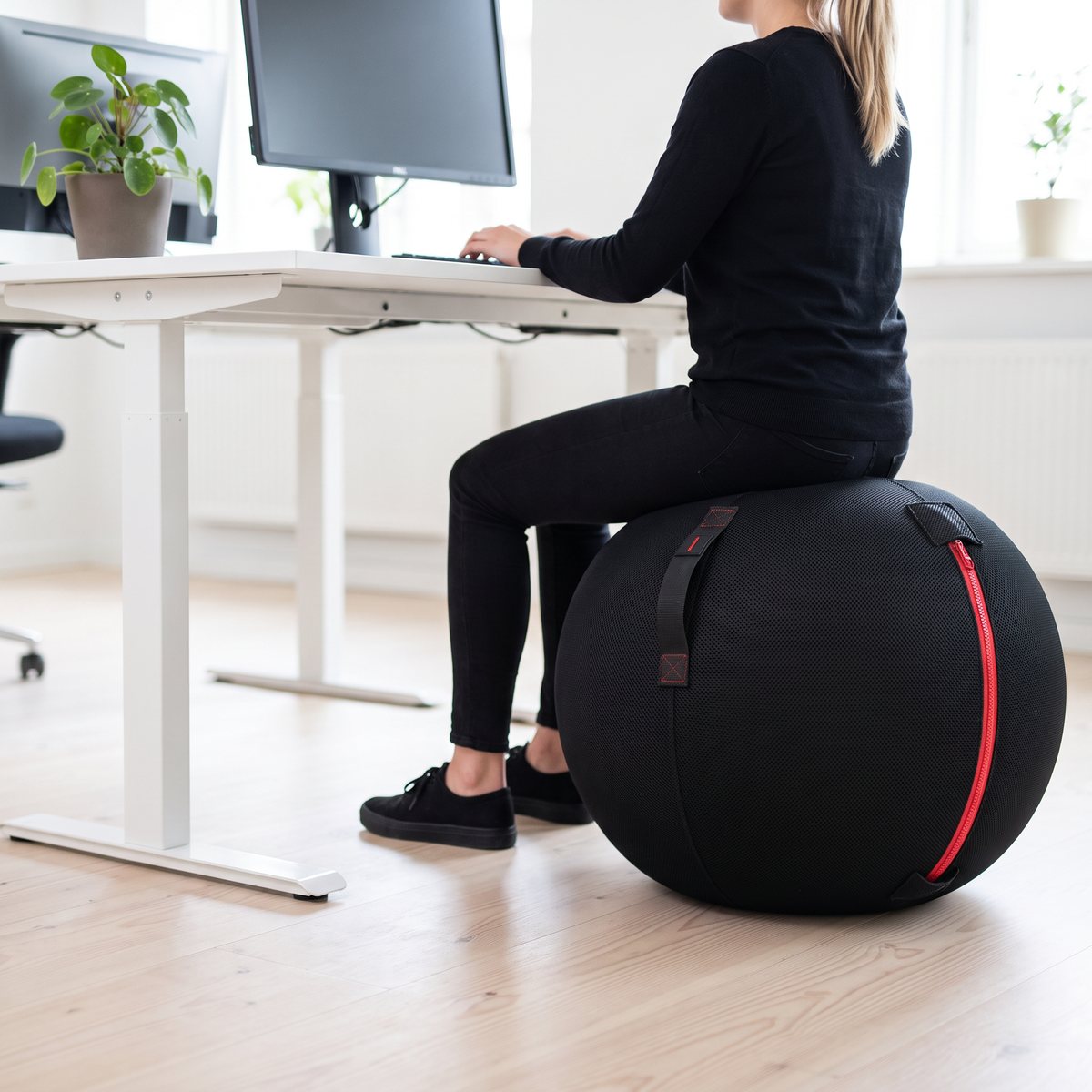 Svart kontorsboll med överdrag och röd dragkedja som arbetsstol vid ett skrivbord