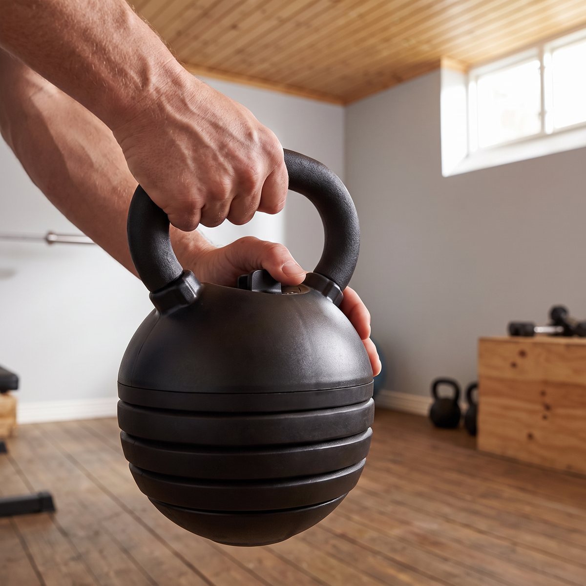 Justerbar kettlebell från Casall som greppas i handtaget medan vikten ställs in med vredet på toppen i ett svenskt källargym