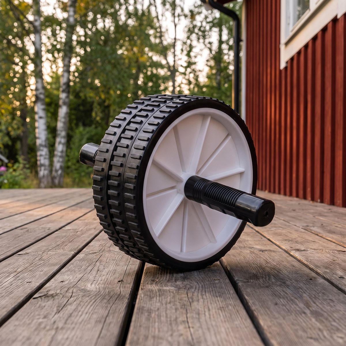 Tunturi Dubbelt Ab Wheel på en trädäck vid en falurödfärgad stuga bland björkar