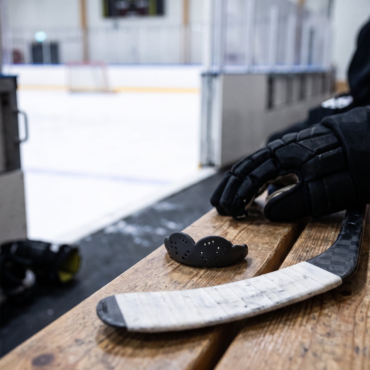 Svart SISU Max tandskydd på en träbänk i en svensk ishall bredvid hockeyklubba och handskar