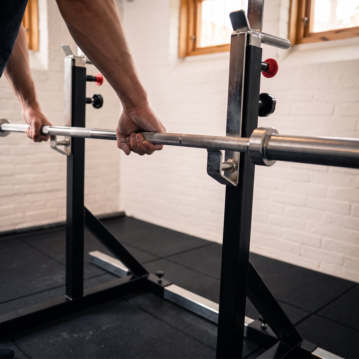 Händer greppar en skivstång i en squatställning i ett svenskt villakällargym med vit tegelvägg