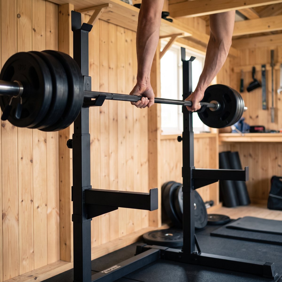Skivstångsställning med skivstång som lyfts ur kroken i ett svenskt garagegym med furupanel