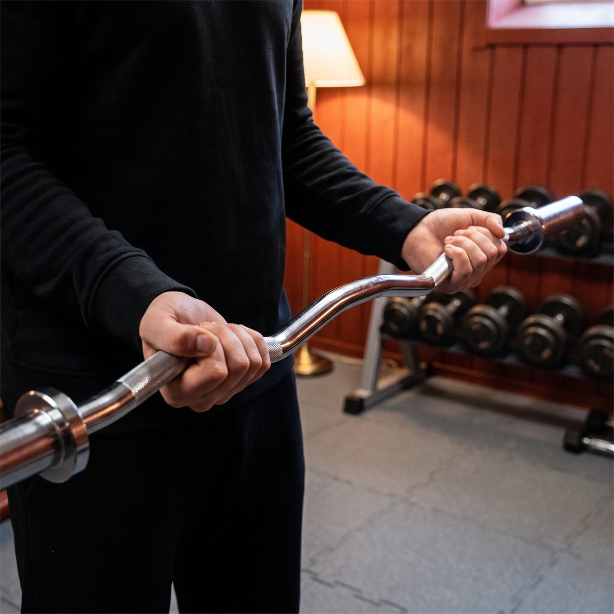 Titan LIFE PRO EZ Curl Bar används vid en bicepscurl i ett svenskt källargym med faluröda träväggar