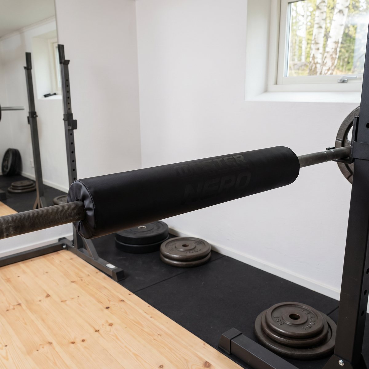 Svart stångdyna från Master Fitness monterad på en skivstång i ett svenskt hemmagym med furugolv och vita väggar