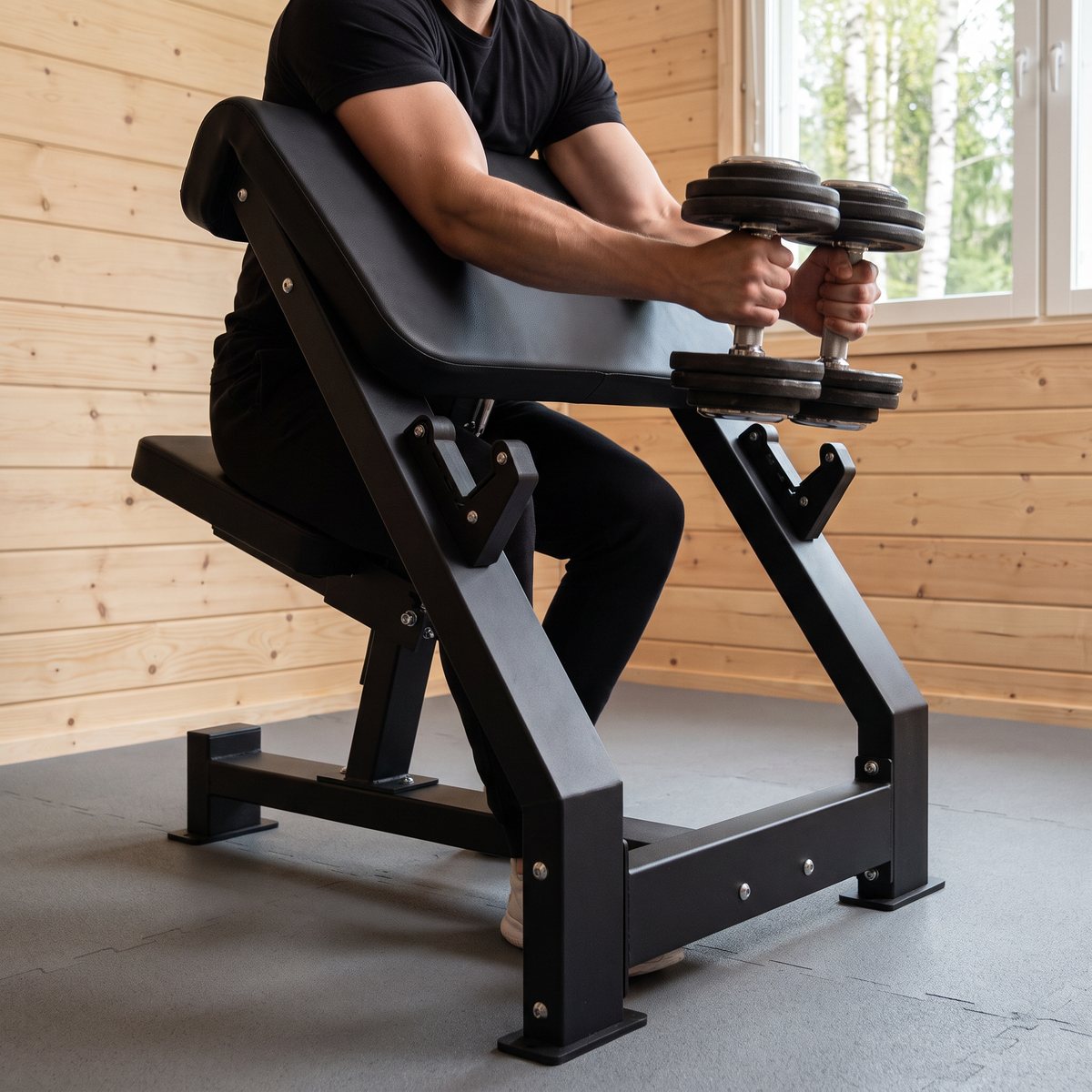 Gymstick Scott Bench Pro i ett hemmagym med ljusa träpaneler och björkar utanför fönstret, där någon tränar bicepscurl med hantlar mot det vinklade armstödet