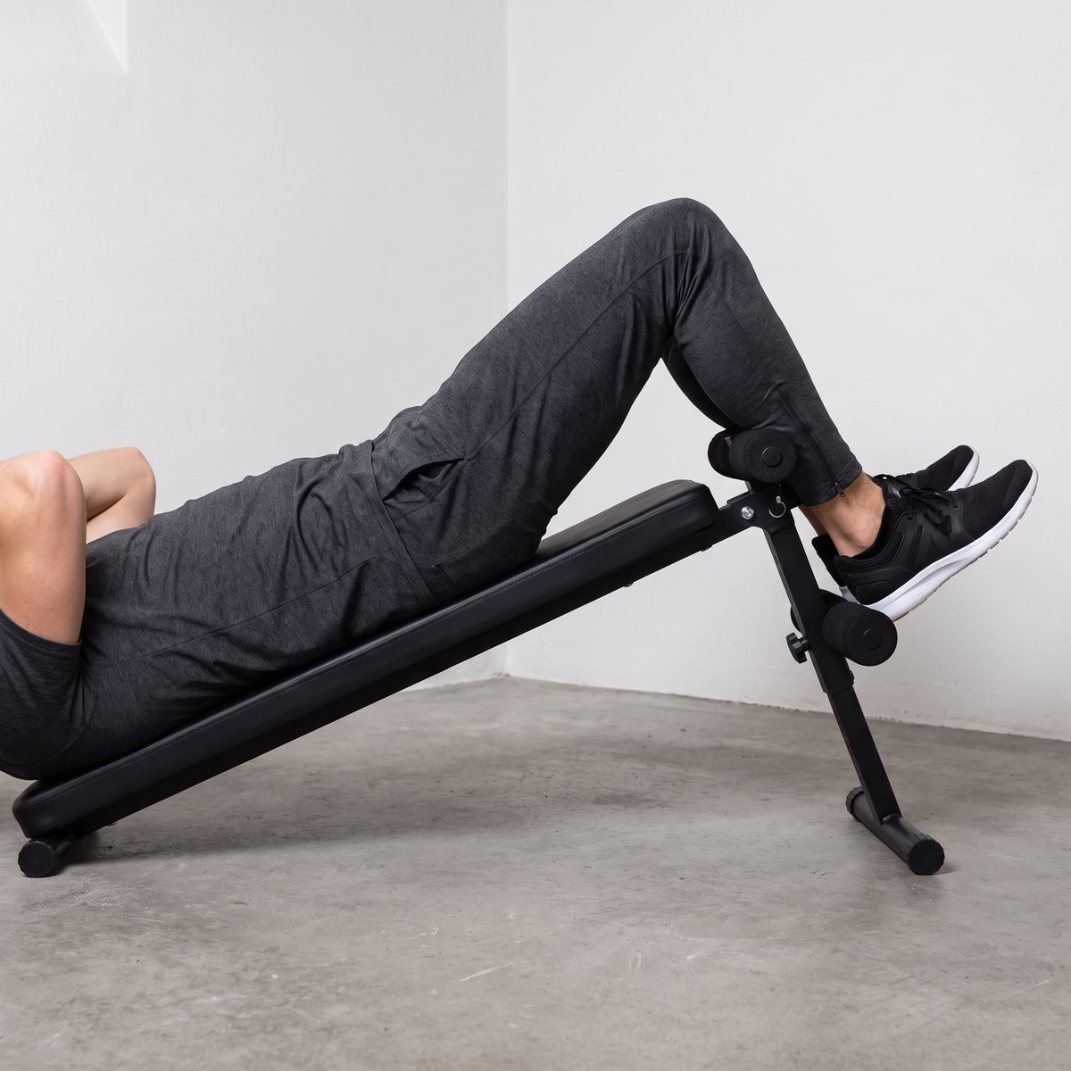 Abilica SitUps 2.0, en svart situpsbänk med lång dyna, används för situps i ett svenskt hobbyrum med betonggolv