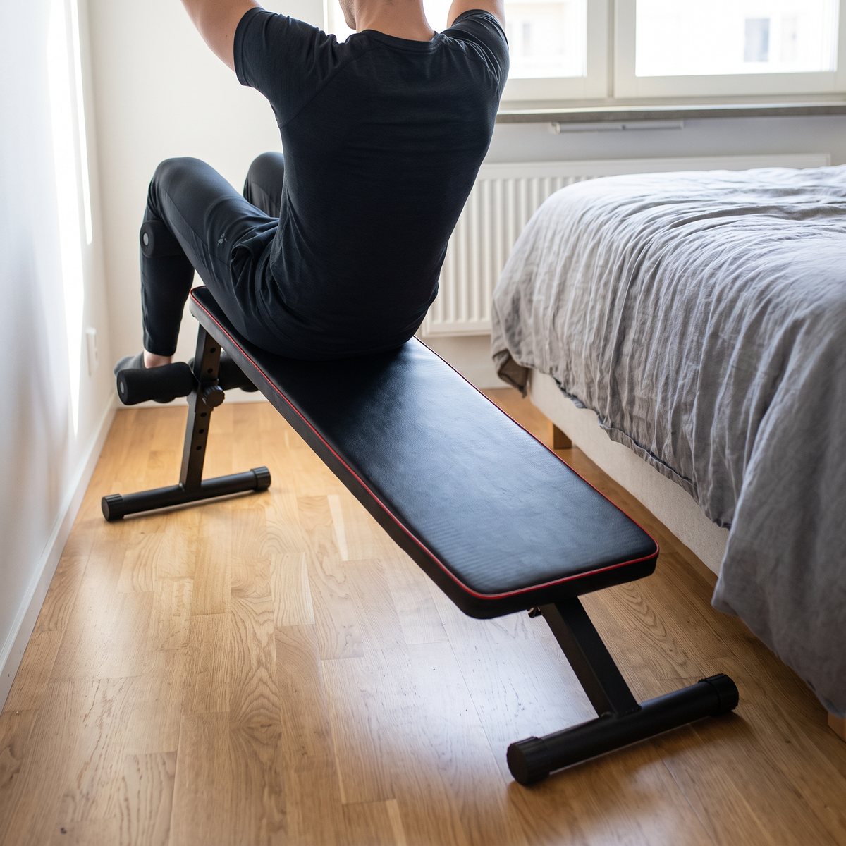Gymstick Abbench, en svart magbänk med röd kant, på ett ljust ekparkettgolv i ett svenskt sovrum