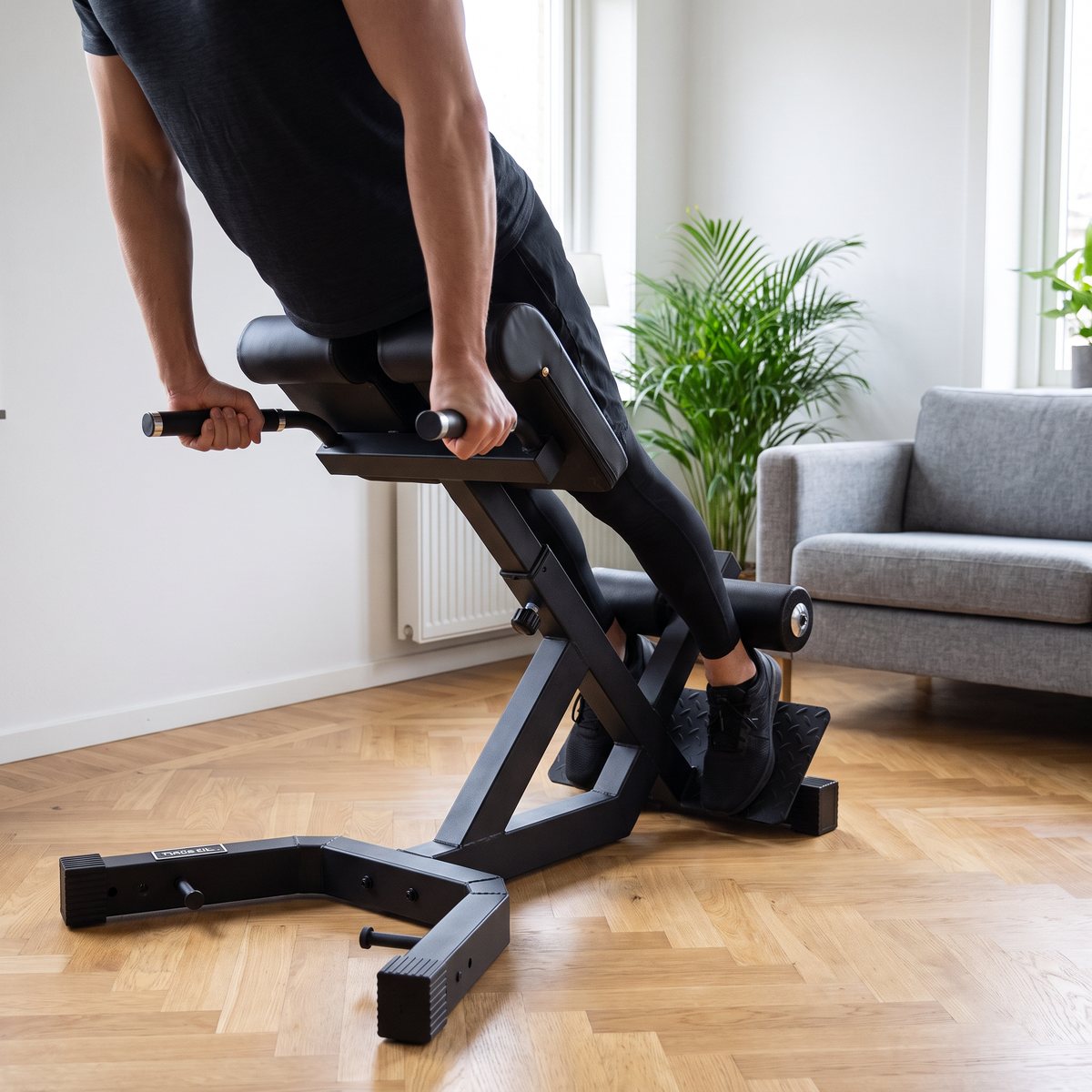 Person gör rygglyft på en svart hyperextensionbänk i stål i ett svenskt vardagsrum med parkettgolv