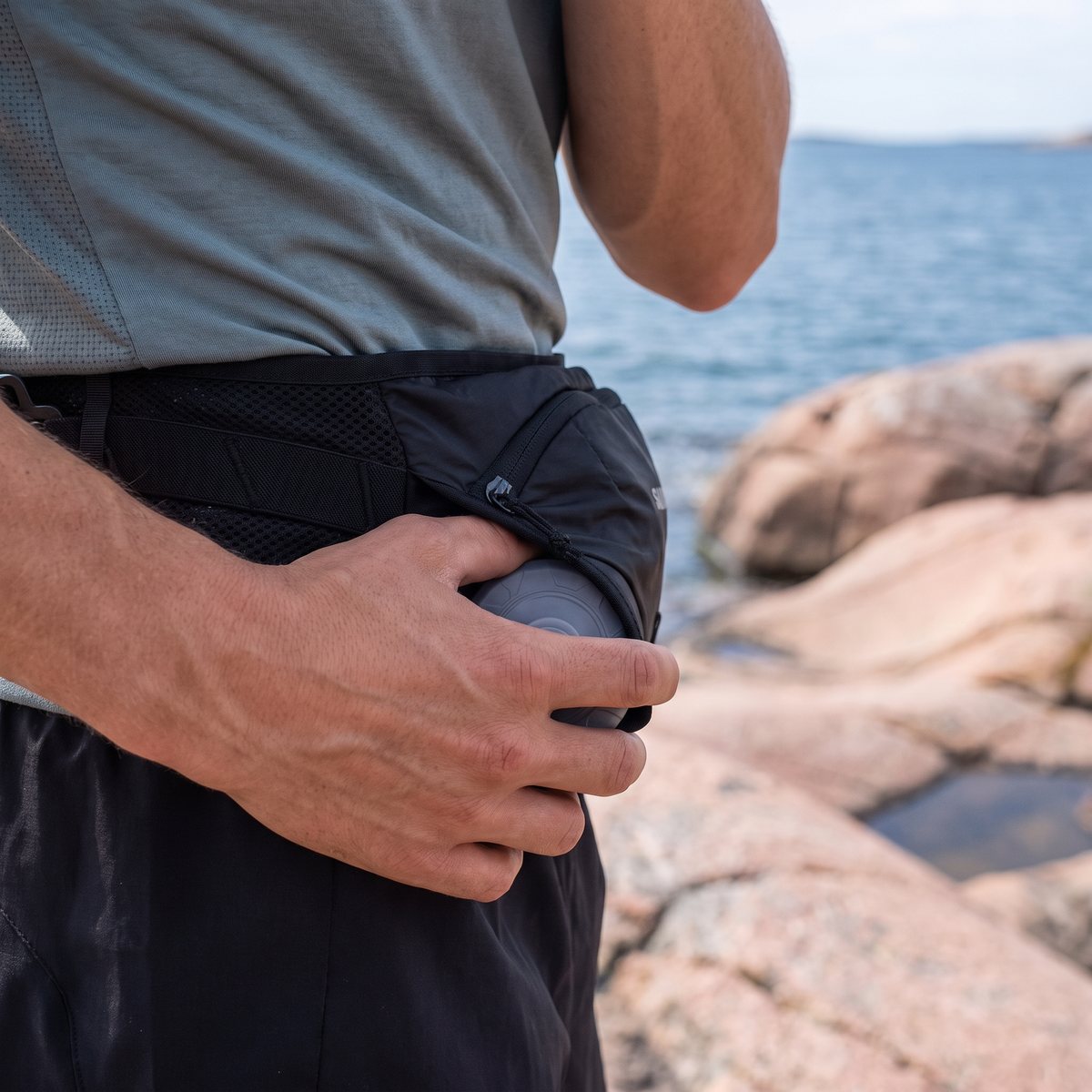 Löpare vid den svenska kusten bland rosa granitklippor med Salomon Cross Belt med en flaska
