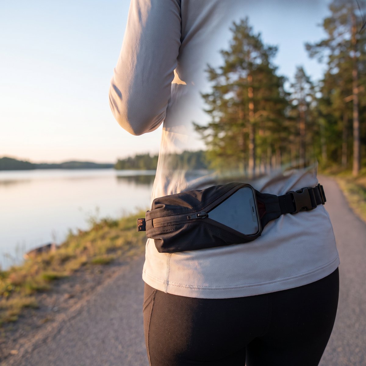 Löpare sedd bakifrån på en asfalterad stig vid en svensk insjö med svart SPIbelt Performance och mobil i fickan