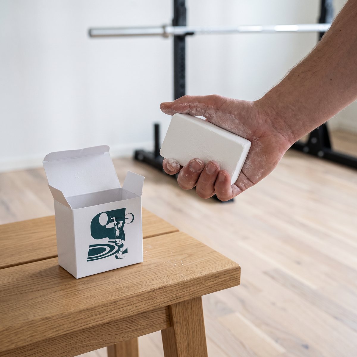 Vitt kritblock i handen bredvid den öppnade lilla kartongen på en träbänk i ett hemmagym