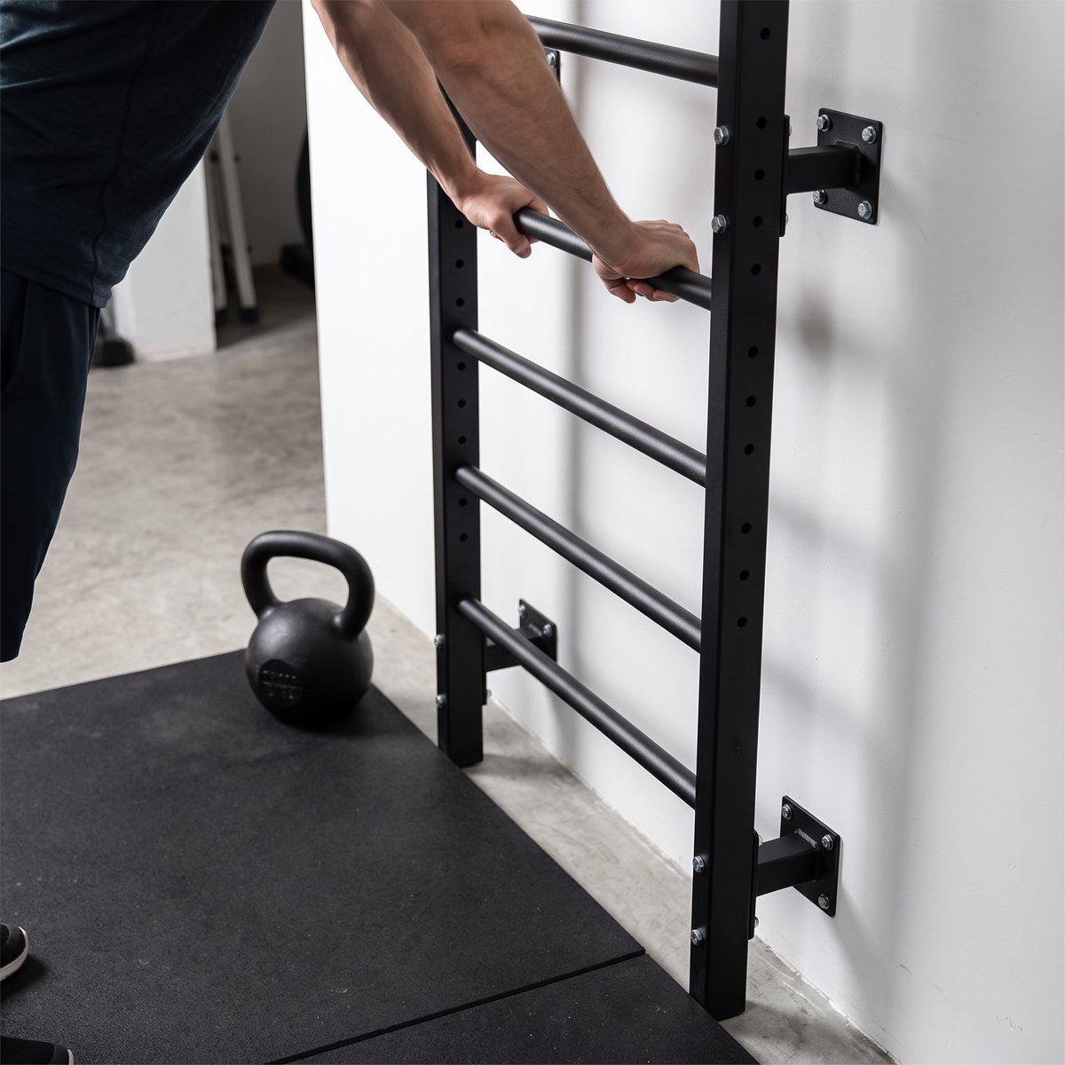 Gymstick Wall Bars Steel ribbstol i svart stål i ett svenskt källargym, en person sträcker sig med händerna på en spjäla