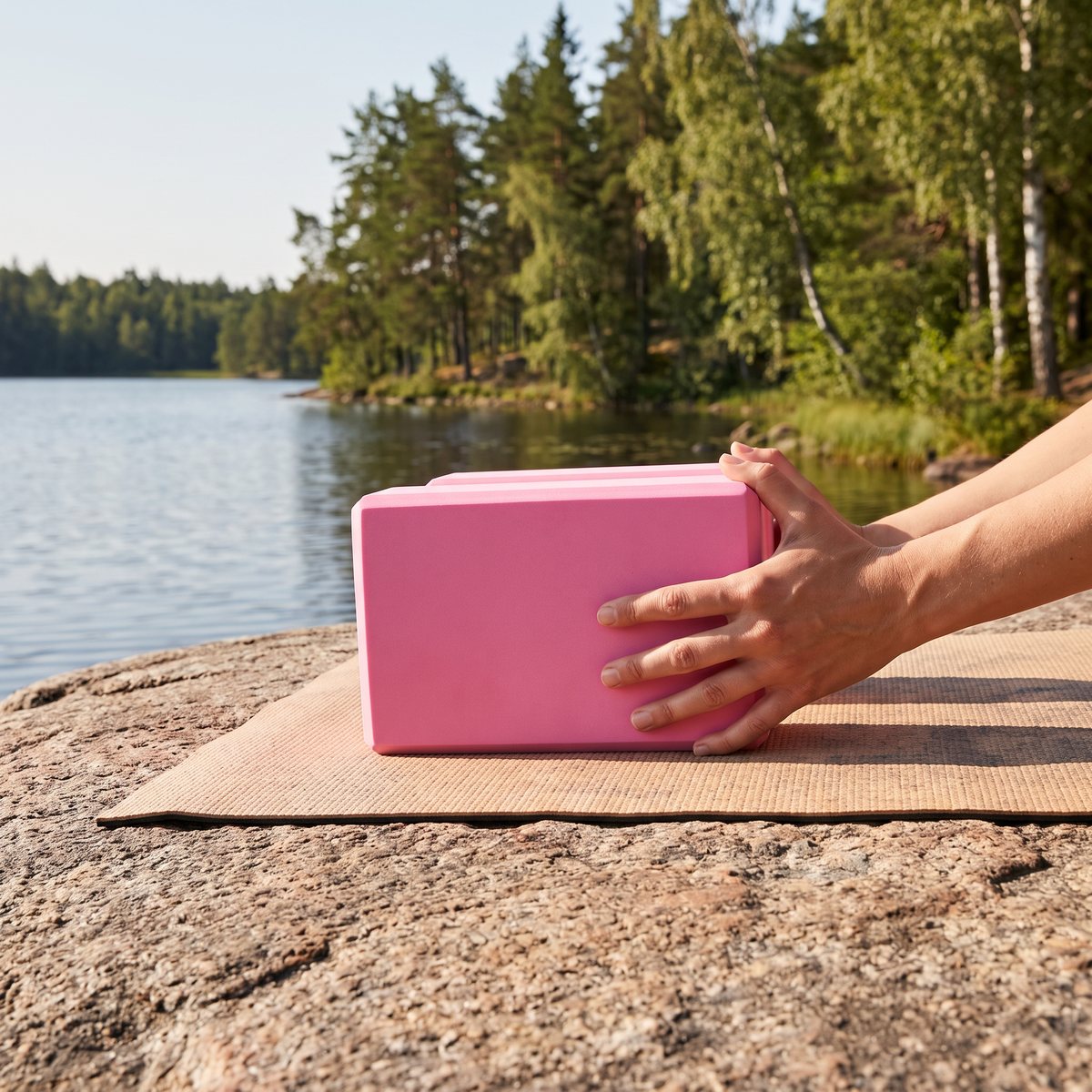 Rosa yogablock i skumgummi vid en stretch på yogamatta på en granithäll vid en svensk sjö